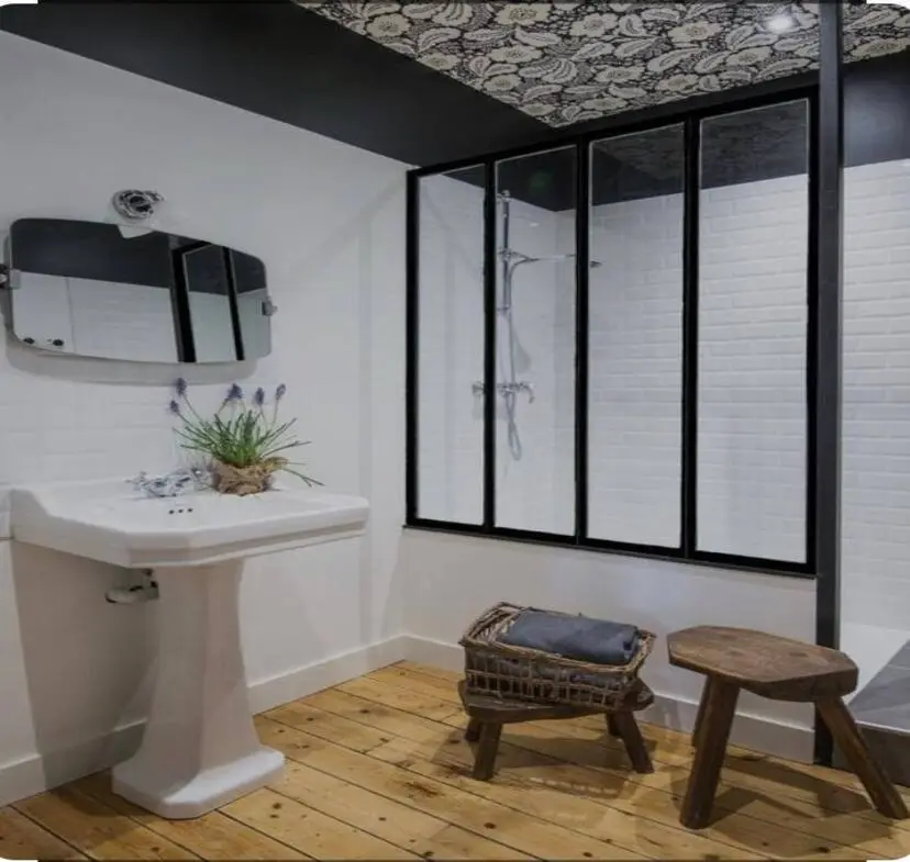 Salle de bain rénovée par CRD Probat avec verrière atelier noire, lavabo sur colonne blanc, parquet bois et tabourets vintage