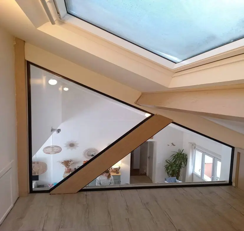 Verrière triangulaire sous fenêtre de toit réalisée par CRD Probat, avec cadres métalliques noirs et spots intégrés
